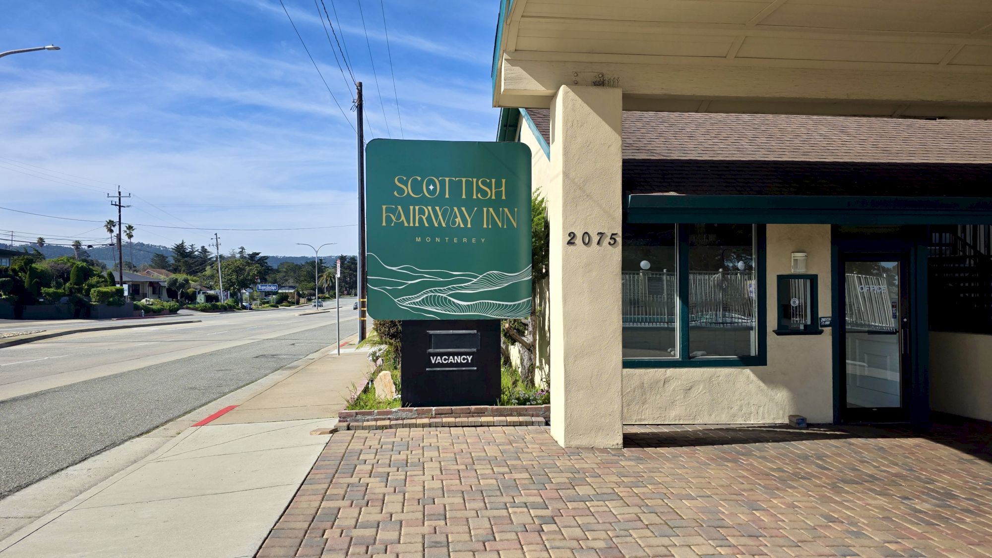 A street view of a Scottish Fairow Inn (Scottish Fairway Inn) with a green sign near the sidewalk and a brick-paved entrance to the building.