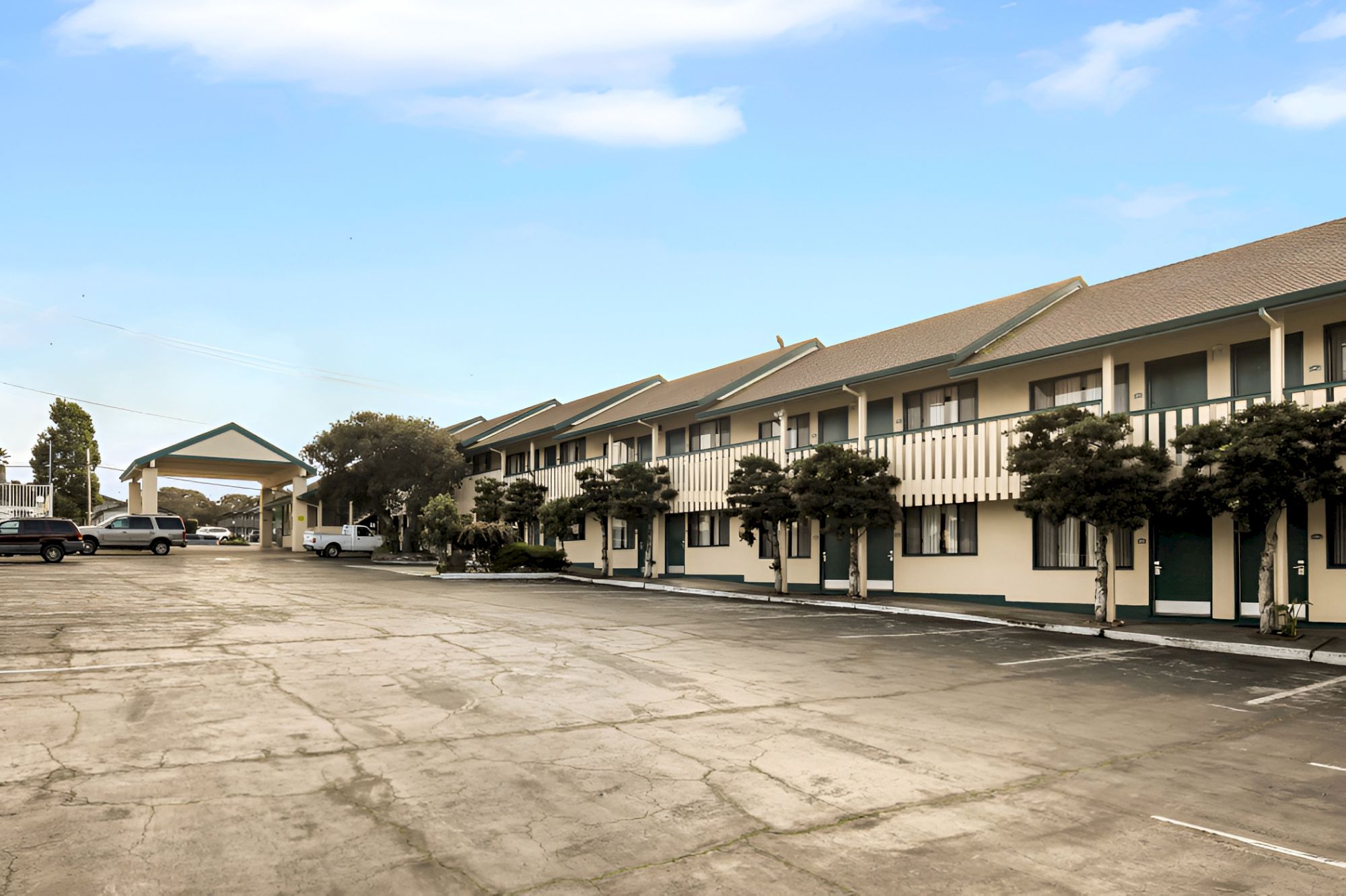A two-story motel with multiple doors facing a long parking lot; a carport/entrance at the far end, under a clear blue sky.
