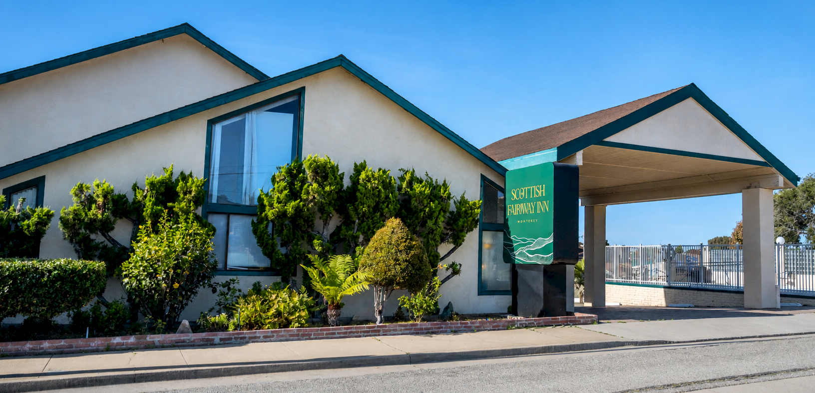 A single-story beige building with a sloped roof, green shrubs, and a green banner reading &ldquo;Customer Pharmacy&rdquo; near the entrance, under a clear blue sky.