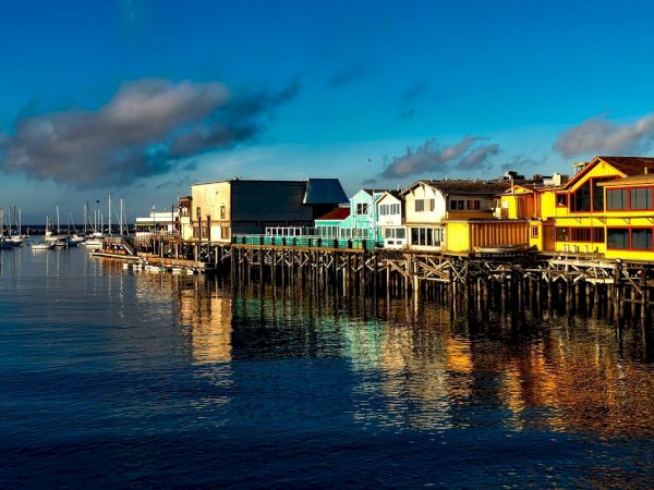 Colorful waterfront houses on stilts along a calm harbor with boats, reflecting in the water.