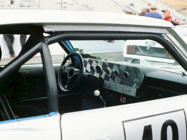 A vintage race car interior with a perforated metal dashboard, classic steering wheel, and a numbered race door display.
