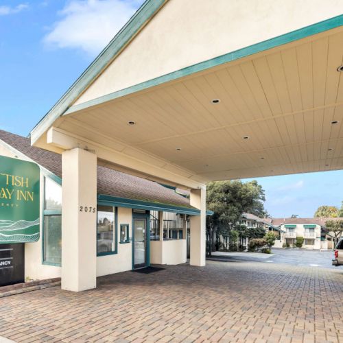 A Scottish-themed hotel sign reads &ldquo;Scottish Fairway Inn&rdquo; beside a covered driveway and line of parked cars at the entrance.