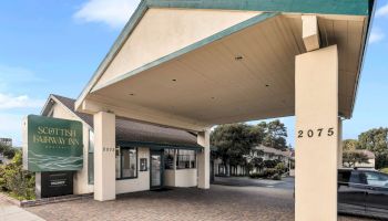 A mid-century hotel entrance with a tall angled roof, green trim, and a large sign reading &ldquo;SCOTT&rsquo;S FAIRWAY INN&rdquo; near the driveway, 2075.